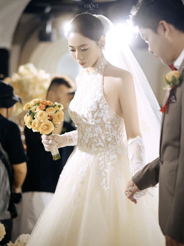 Váy cưới cổ yếm ren hoa nhẹ, dáng chữ A mềm mại, tôn vai và cổ cao.